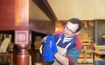 Artesão aplicando acabamento de cera em móveis