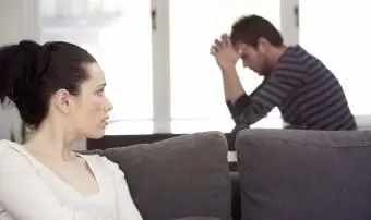 Mladá žena sedí na pohovke a pozerá sa na nešťastného muža pri stole