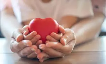 Mani di adulto e bambino che tengono il cuore rosso