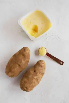 2 whole potatoes, a container of fat, and a teaspoon with fat on it
