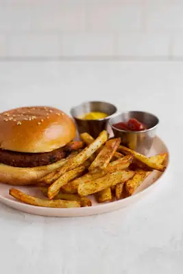 a pink plate with a hamburger, air fried seasoned french fries, a cup of mustard, and a cup of ketchup