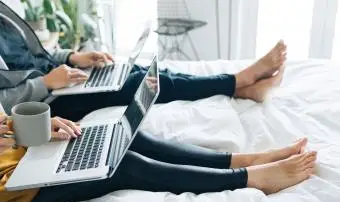 pár v posteli pracující na přenosných počítačích