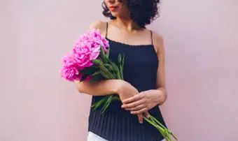 Femme tenant un bouquet tout en posant contre un mur de fond rose