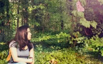 Frau sitzt auf efeubewachsenem Boden und betrachtet einen Schmetterling