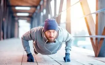 Mężczyzna w kapeluszu i bluzie robi pompki na świeżym powietrzu