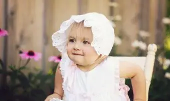 Bambina seduta sulla vecchia sedia di legno che indossa abiti vintage