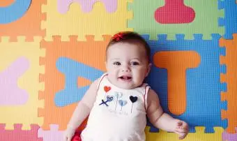 Roztomilá holčička odpočívá na barevné abecední puzzle hrací podložce