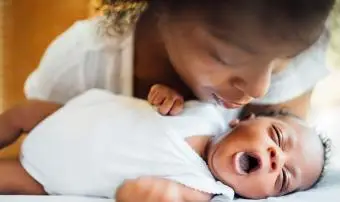 matka se dívá na roztomilou novorozenou dceru zívající vleže na posteli