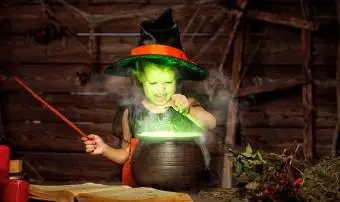 Malá čarodějnice dítě vaření lektvaru v kotli s knihou kouzel