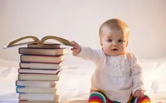 Dítě sedí v posteli s hromadou knih