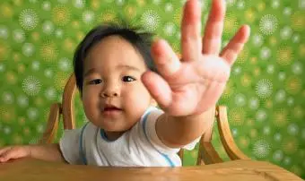 Chlapček (9-12 mesiacov) sedí na vysokej stoličke s natiahnutou rukou