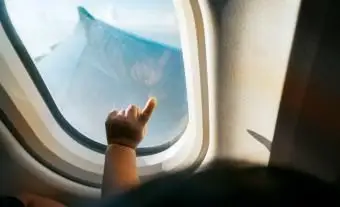 여행하는 동안 푸른 하늘을 배경으로 비행기 창을 가리키는 유아의 손