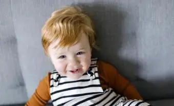 Souriant petit garçon aux cheveux rouges sur canapé