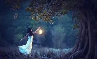 Bella ragazza in bianco che tiene una lanterna nella foresta autunnale che brilla sotto gli alberi