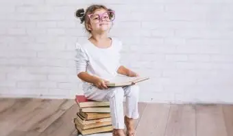 Kind kleines Mädchen sitzt auf einem Stapel Bücher mit Brille books