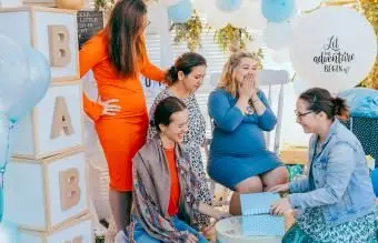 Amigas abrem caixas de presente com uma mulher grávida em um chá de bebê
