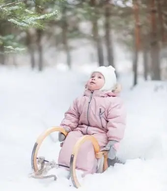 Mała dziewczynka siedząca na saniach w zimowym lesie