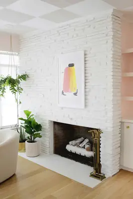 white stone fireplace with art hanging on it and hanging plant nearby