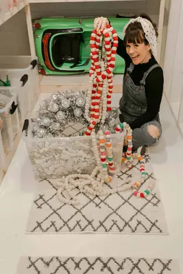 Elsie pulling Christmas decorations out of a clear bin while sitting on the floor of the storage room
