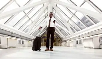 איש לובש לבוש רשמי עומד בשדה תעופה עם מזוודות