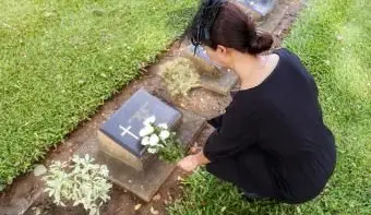 Frau mit Blumen neben einem Grabstein