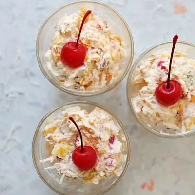 creamy ambrosia fruit salad in three small cups with a cherry on top
