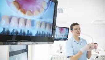 Dentiste portant des lunettes de sécurité et tenant du matériel dentaire à côté d'écrans montrant des images de dents