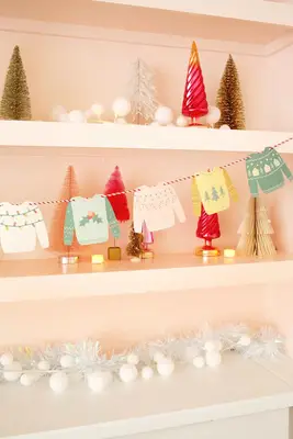 Paper Christmas sweaters strung on a twine string from a shelf with Christmas decor around it
