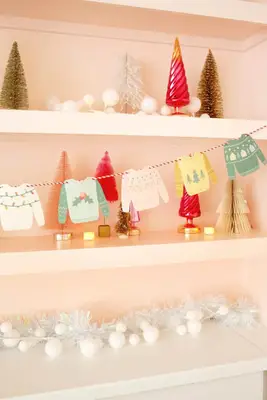 paper christmas sweater garland hung on shelf with christmas trees