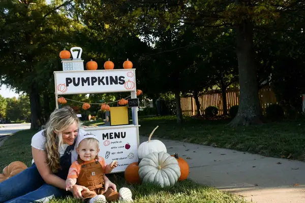Mom and child sitting in front of pumpkin stand.