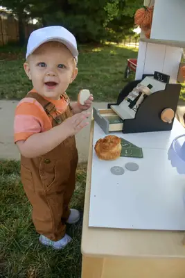 Child holding a cookie and playing with a toy cash register.