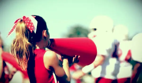 Pom-pom girl avec mégaphone et joueurs en arrière-plan