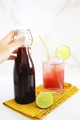 Bottle of homemade grenadine next to a cocktail