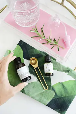 a tray with a pitcher of water and a spray bottle on it with the bottle of Solubol, the bottle of Rosemary essential oil, and a tablespoon laying next to it