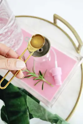 someone holding a tablespoon of liquid over a silver funnel over the spray bottle