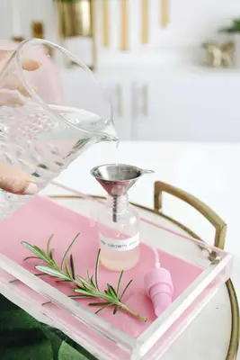 someone puring water from pitcher into the silver funnel into the spray bottle