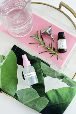 a tray with a pitcher of water, a silver funnel, and a bottle of Rosemary essential oil on it with the spray bottle of hair growth spray laying next to it