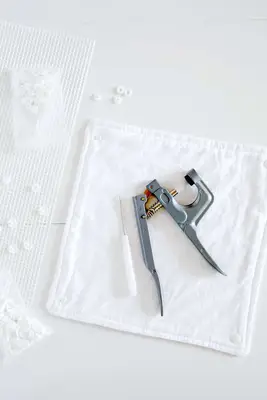 square of cotton fabric with snaps and snap setter on top