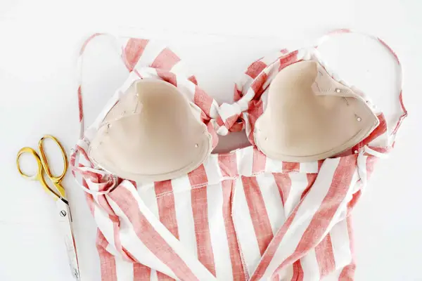 a pink and white stripped dress with bra cups pinned into it and gold scissors laying next to it