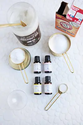 coconut oil with a spoon in it, box of baking soda, a measuring cup with coconut oil in it, a measuring cup with baking soda in it, 4 bottles of essential oils, a tablespoon, and a clear ball