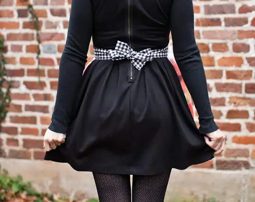 the back of a woman in a black dress with the apron tied around her