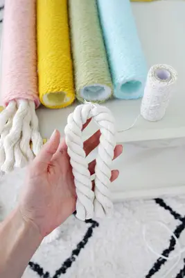 4 yarn wrapped pool noodles, 1 with heavy rope hanging out the end of it, and a hand holding the heavy rope