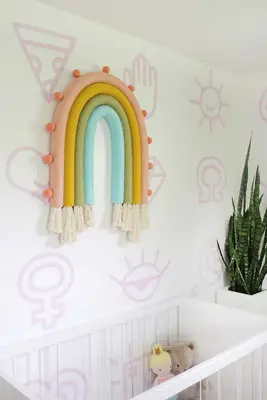 nursery with a white crib, plant, and a rainbow wall hanging on the wall above the crib