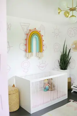 a nursery with a white crib, a plant, and the rainbow wall hanging above the crib