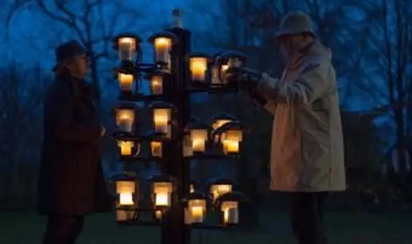 Zwei Erwachsene zünden auf dem Friedhof Kerzen an