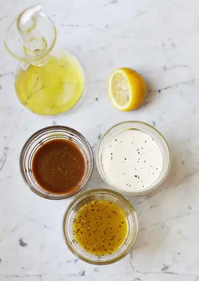3 glass bowls of sauces, half a lemon, and a glass bottle of yellow liquid