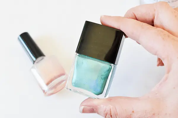 someone holding a teal bottle of nail polish with a pink bottle of nail polish laying next to it
