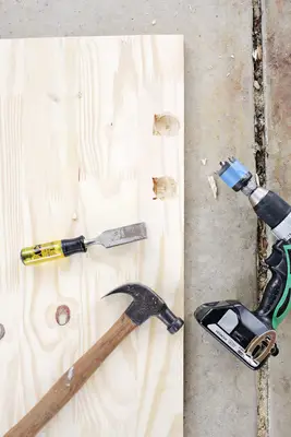 a big piece of wood on the ground with a hammer, drill, and chisel on it