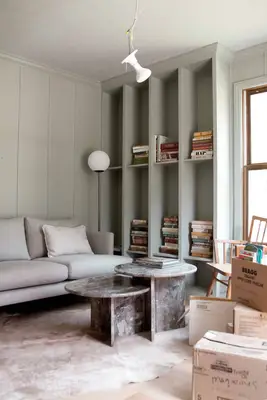 finished bookcase with piles of books on it, light fixture hanging from ceiling, boxes all over floor, gray coach, and coffee table