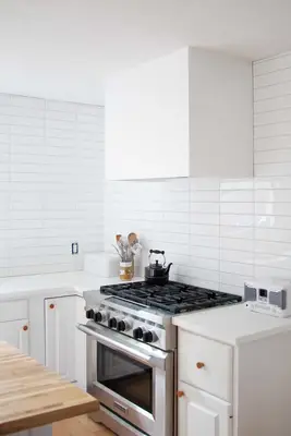 white modern hood vent cover over a stainless stove in a white kitchen